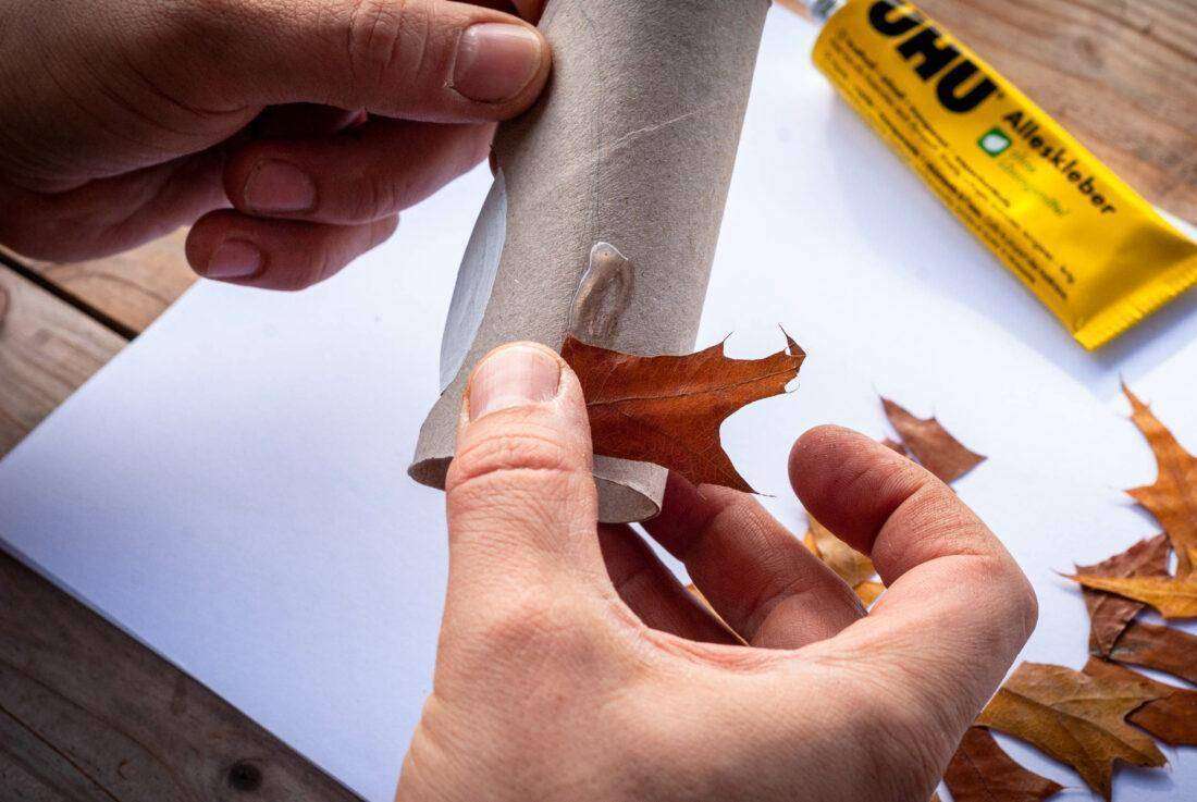 Ein Mann klebt Laub auf eine Papprolle, um daraus einen Igel zu basteln. 