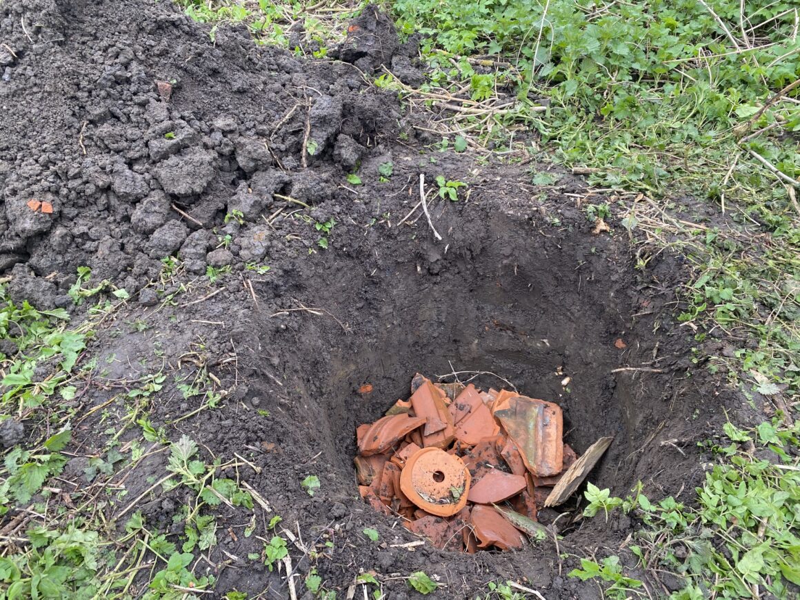 Blick in ein Loch mit einer Drainageschicht aus Tonscherben. Das Loch soll später ein Käferkeller werden. 