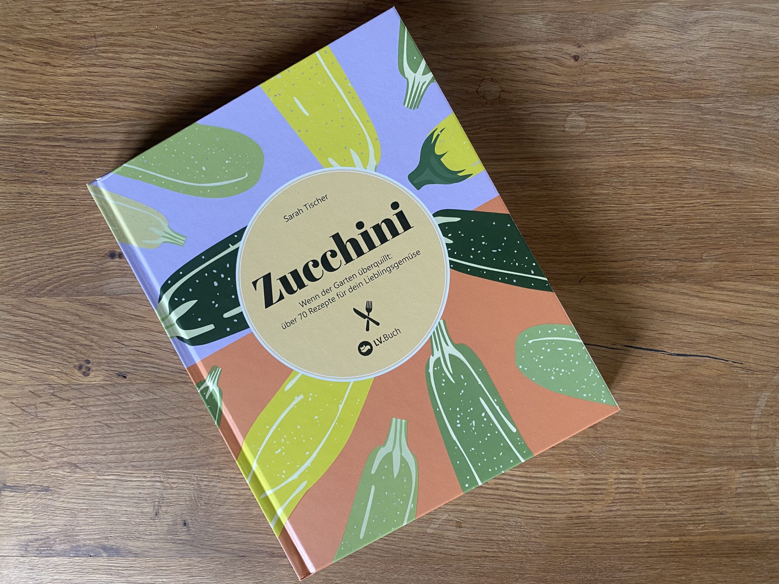 Das Buch Zucchini von Sarah Tischer liegt auf einem Tisch aus Eichenholz